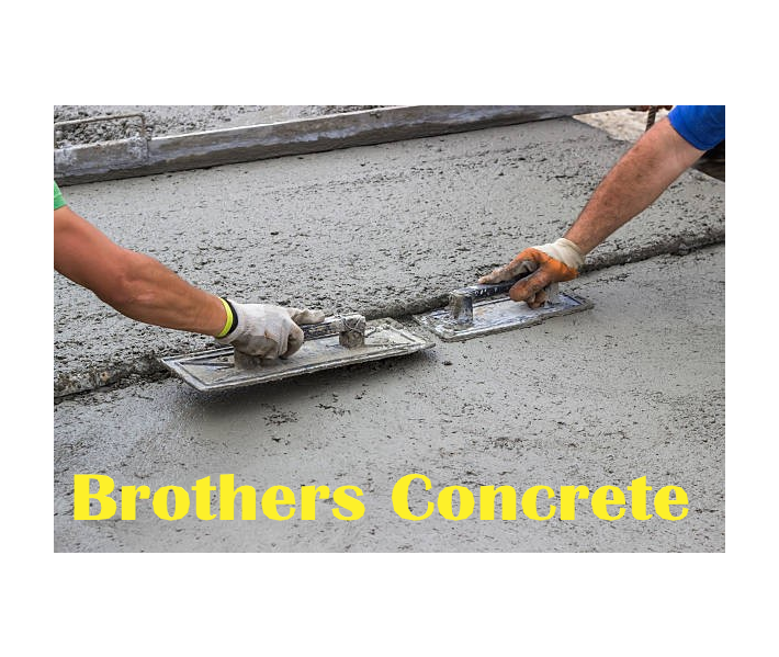 Two men are spreading concrete on a sidewalk with a trowel.