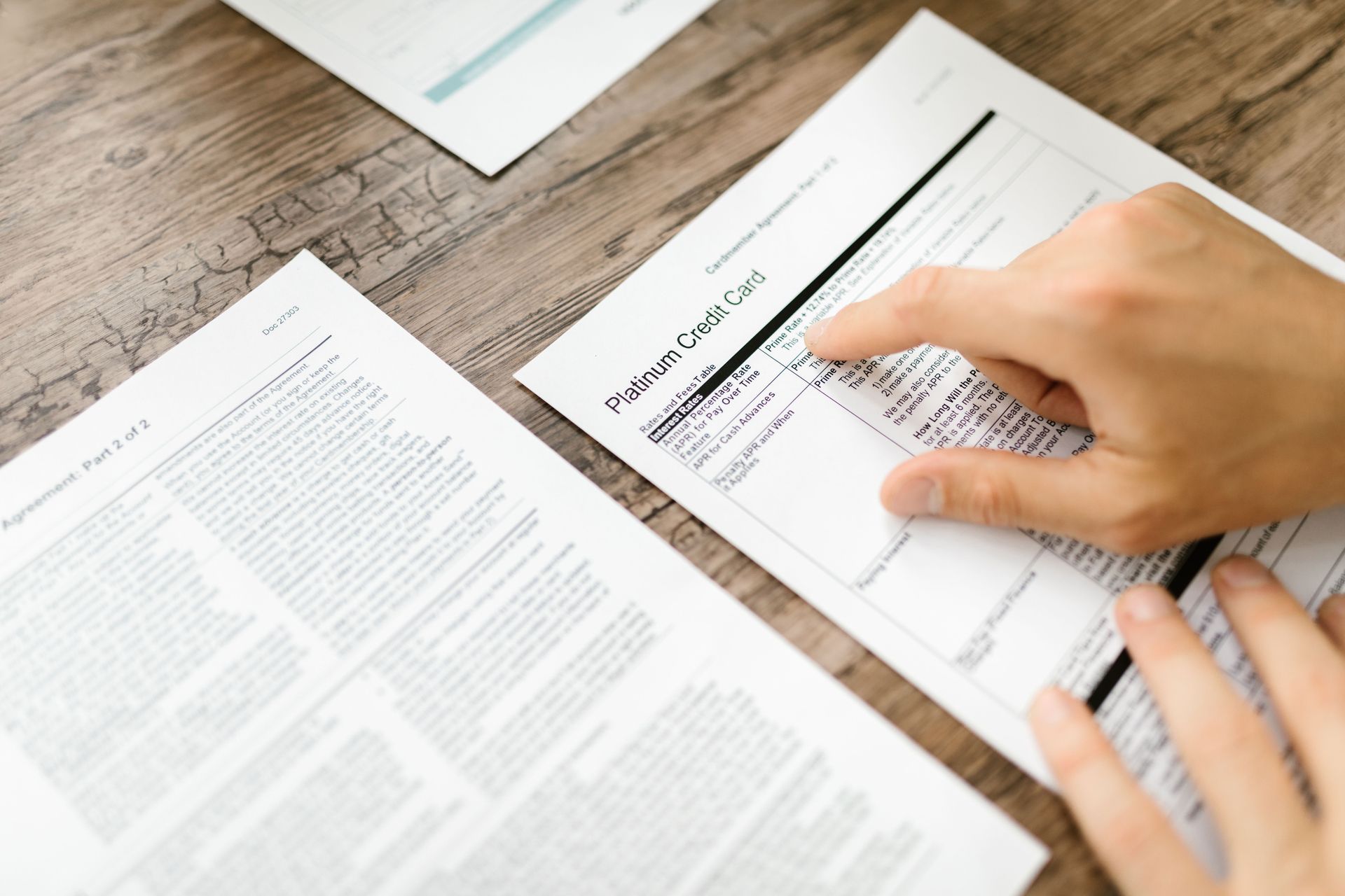 Hands filling out a black-and-white form on a desk beside an open document.