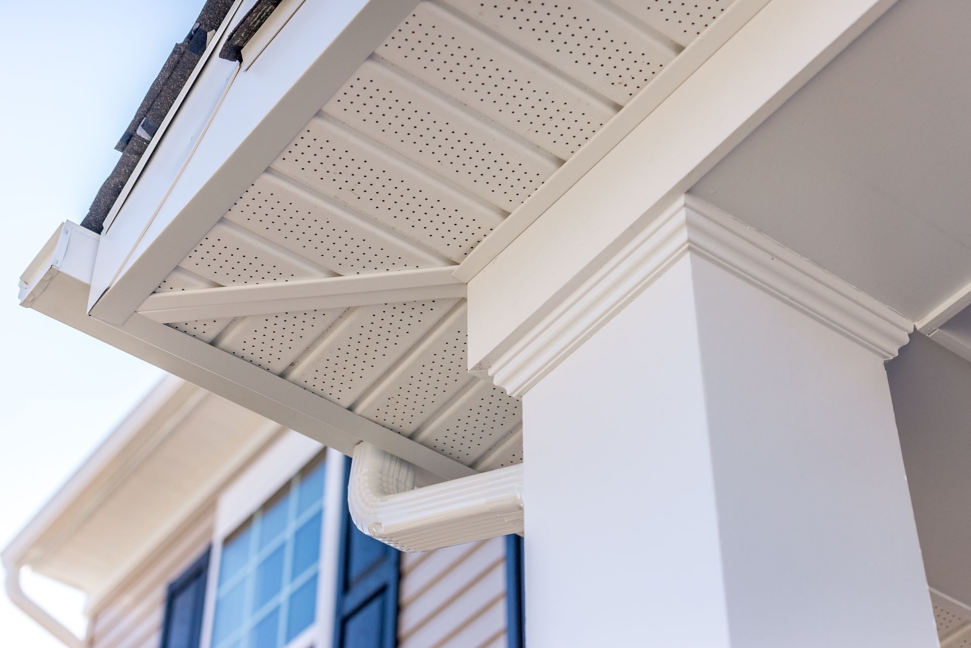 Close-up of white house eaves and decorative soffit above a window and column