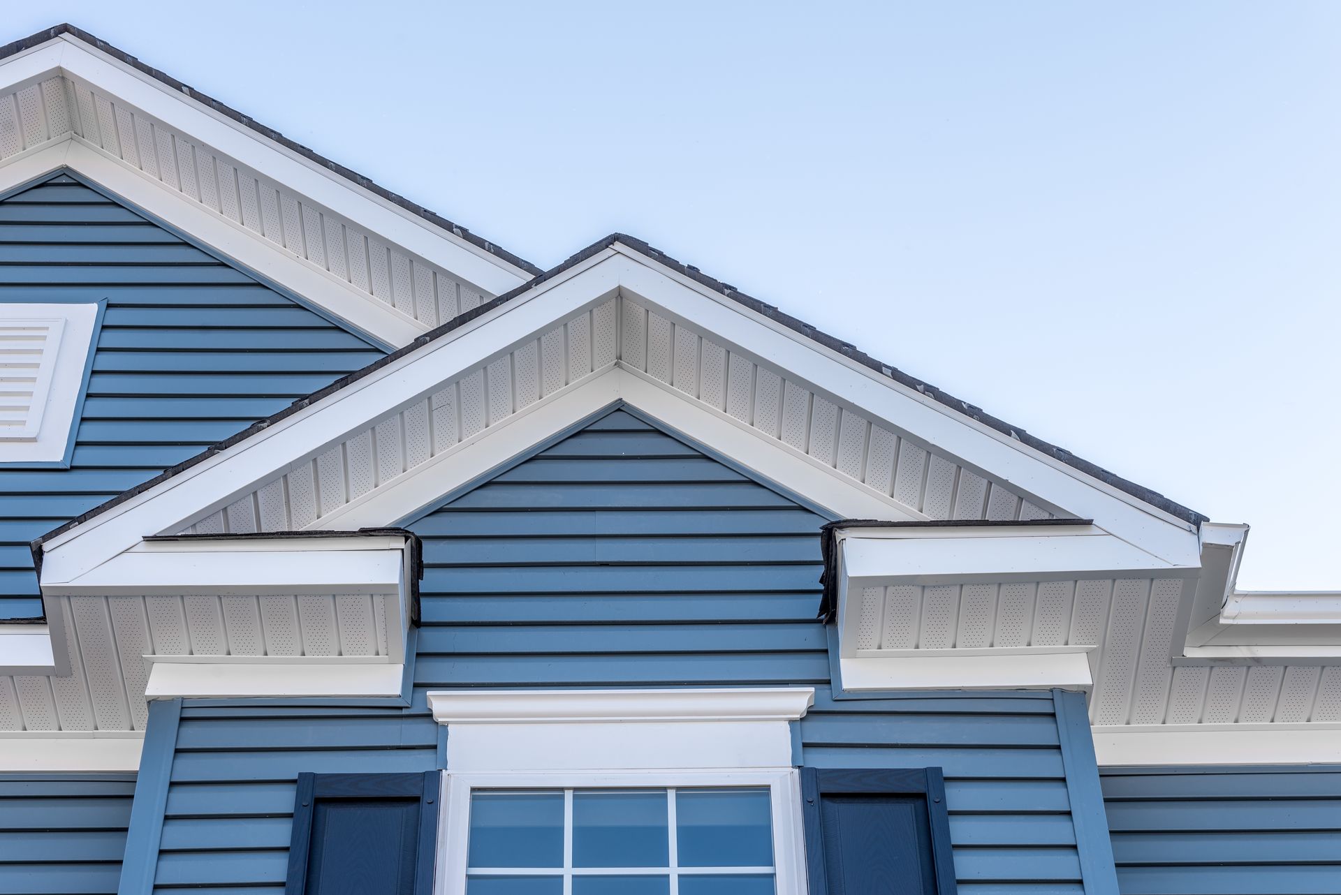 Blue house gables with white trim and a window against a pale sky