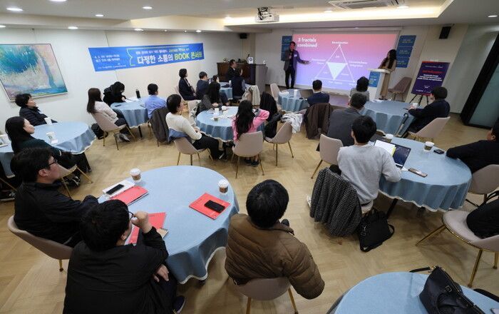 People at a conference, seated around round tables. Speakers on a stage with a presentation.