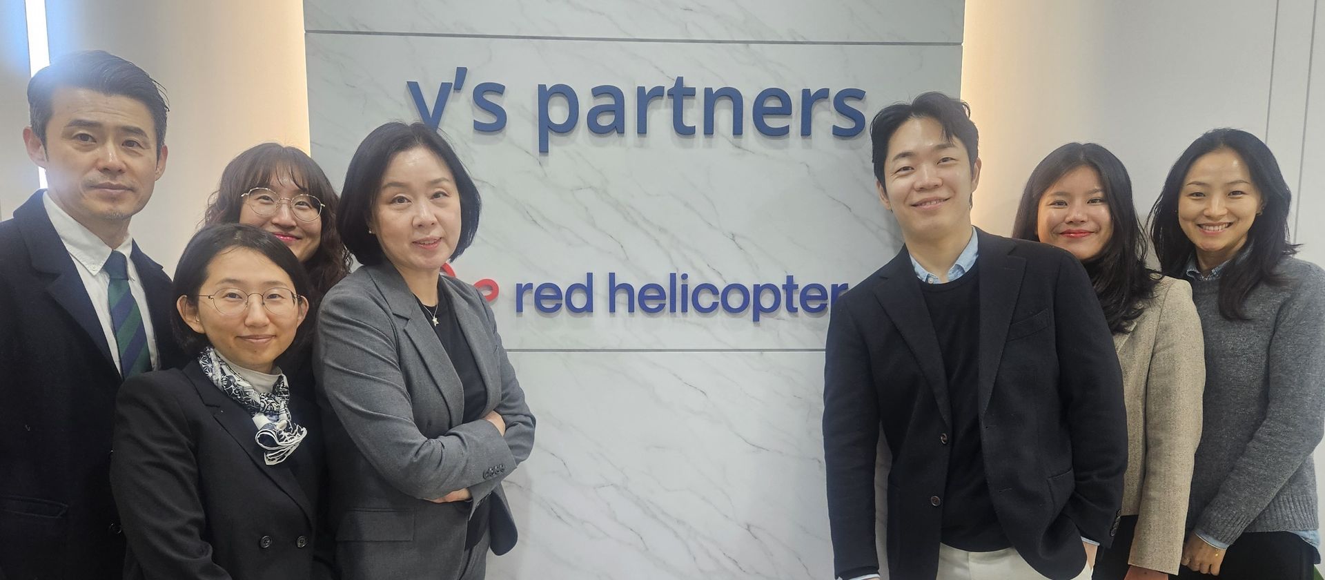 Man in black jacket and woman with red hair holding a book; standing next to a poster; smiling.