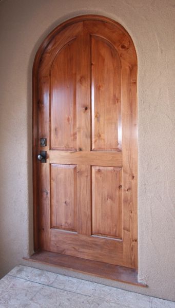 A wooden door with an arched top is sitting on a tiled floor.