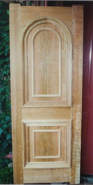 A wooden door is sitting in front of a red door.