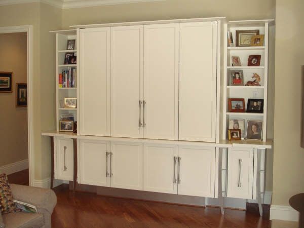 A living room with lots of white cabinets and shelves