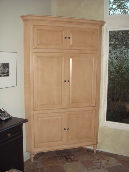 A large wooden cabinet is in the corner of a room next to a window.