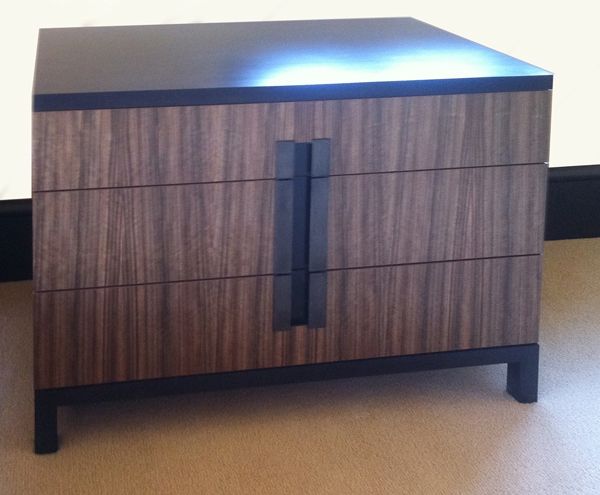 A wooden nightstand with three drawers and a black top