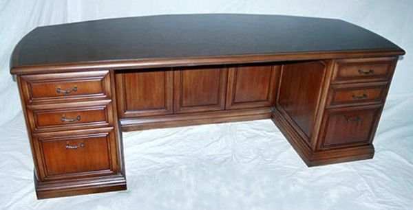 A wooden desk with a curved top and drawers
