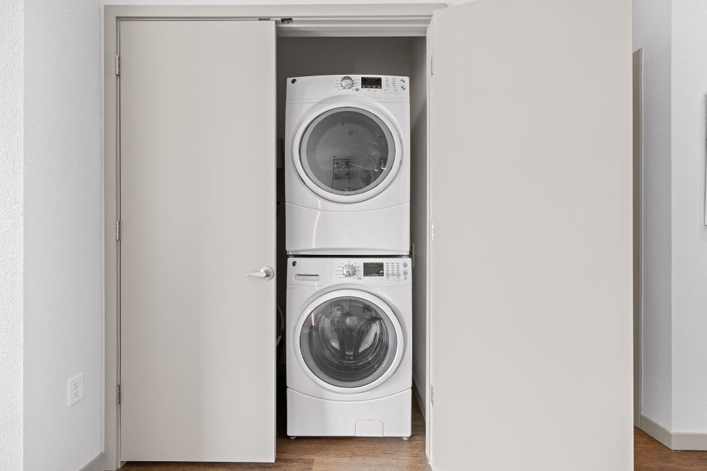 Stacked white washer and dryer in a small laundry closet with open bi-fold doors in a residential home, set against a clean, white interior wall at Marq Iliff Station in Aurora, CO.