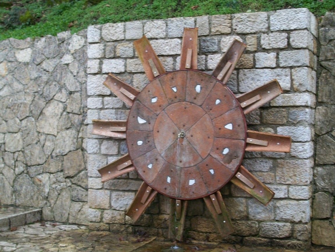 Una ruota idraulica è posizionata davanti a un muro di pietra