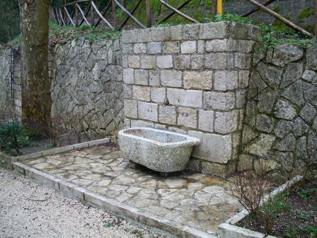 Una fioriera in pietra è posta di fronte a un muro in pietra.