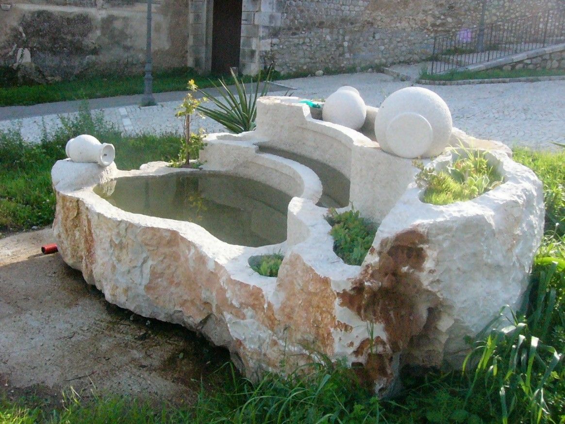 Una grande fontana di pietra si trova nell'erba di fronte a un edificio.