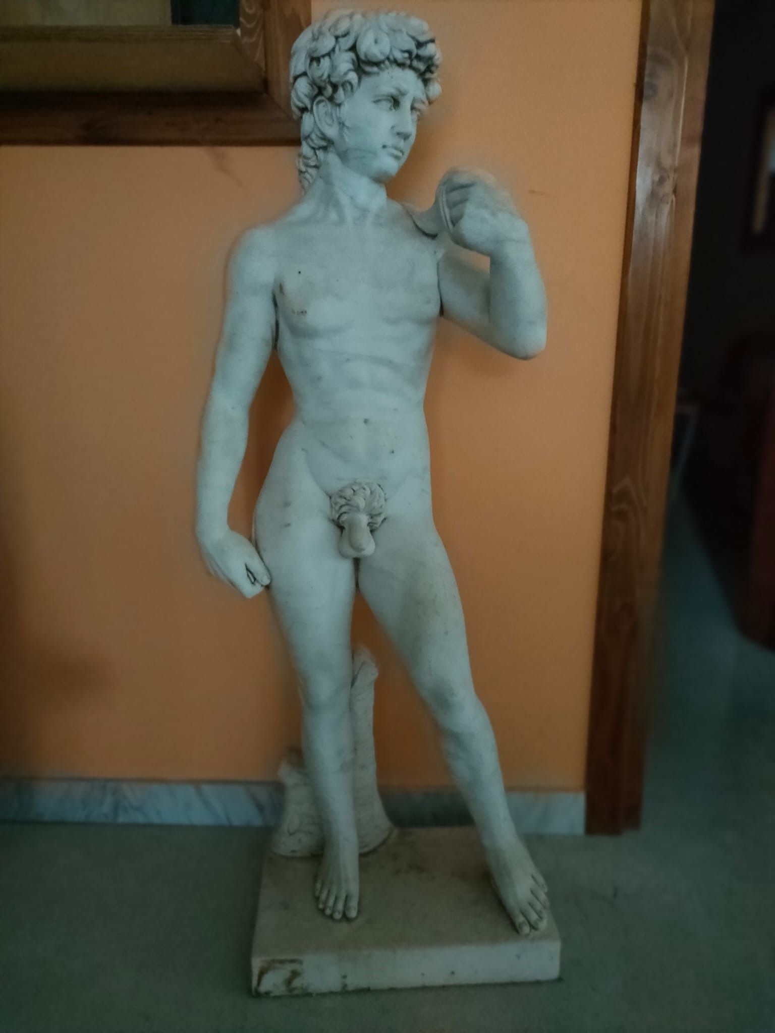 Una statua di un uomo senza camicia è in piedi davanti a un muro arancione