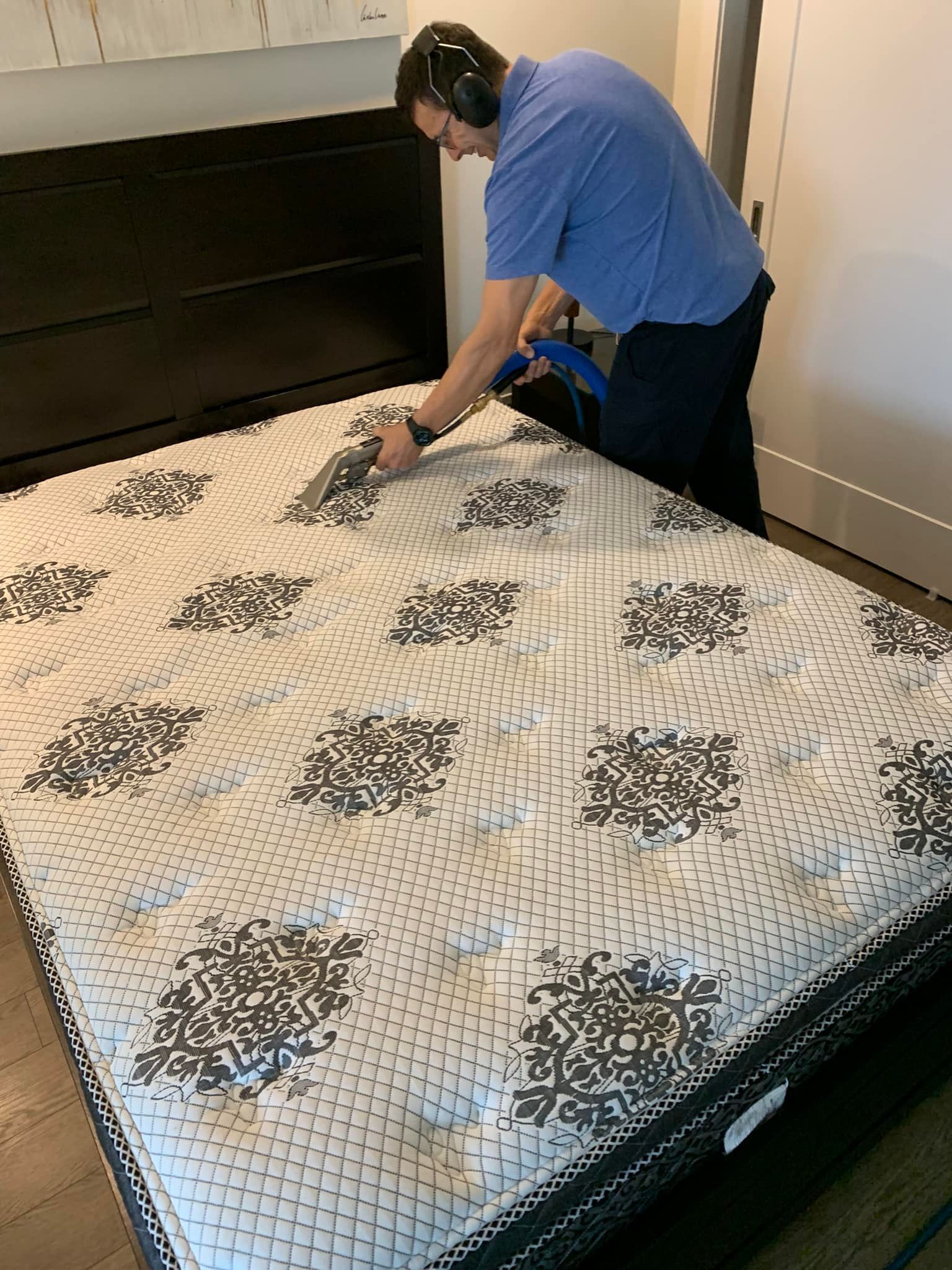 A man is cleaning a mattress with a vacuum cleaner.