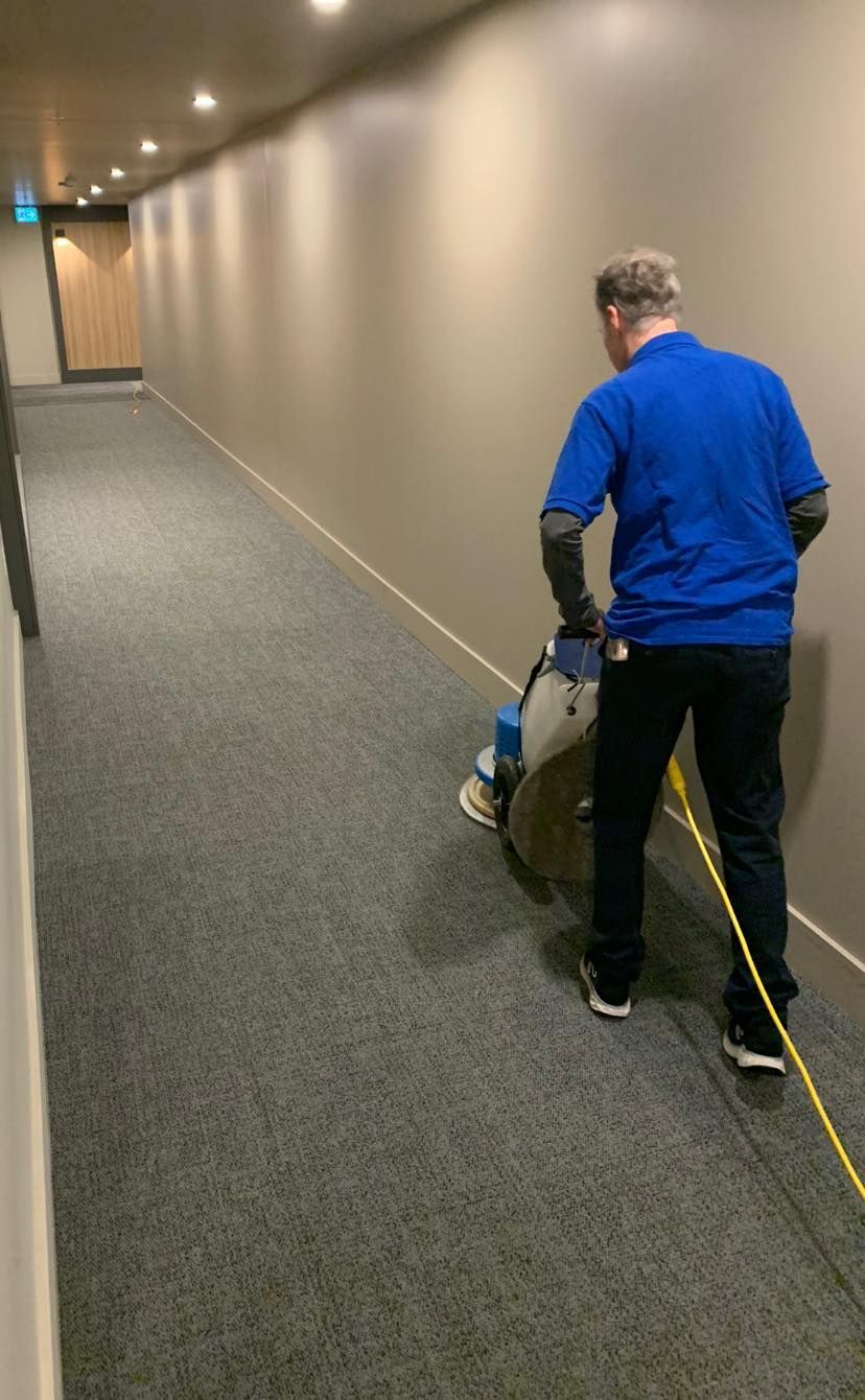 A man is cleaning a hallway with a machine.