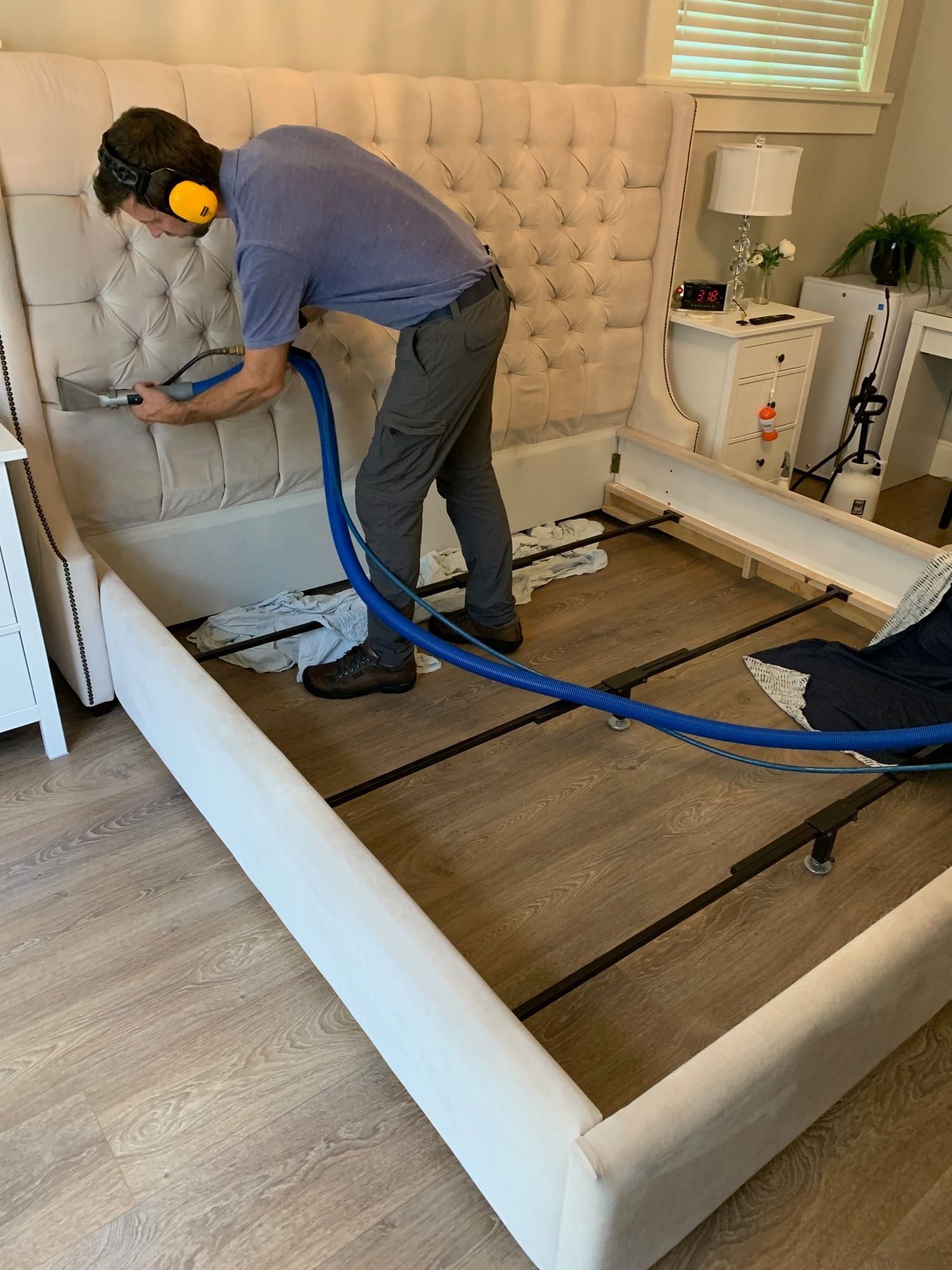 A man is cleaning a bed with a vacuum cleaner.