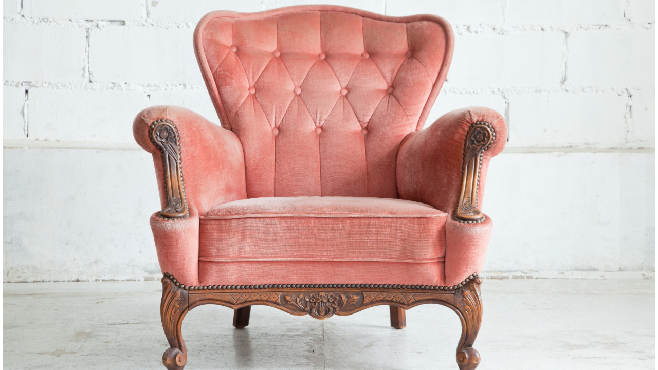 A pink chair is sitting in front of a white wall.