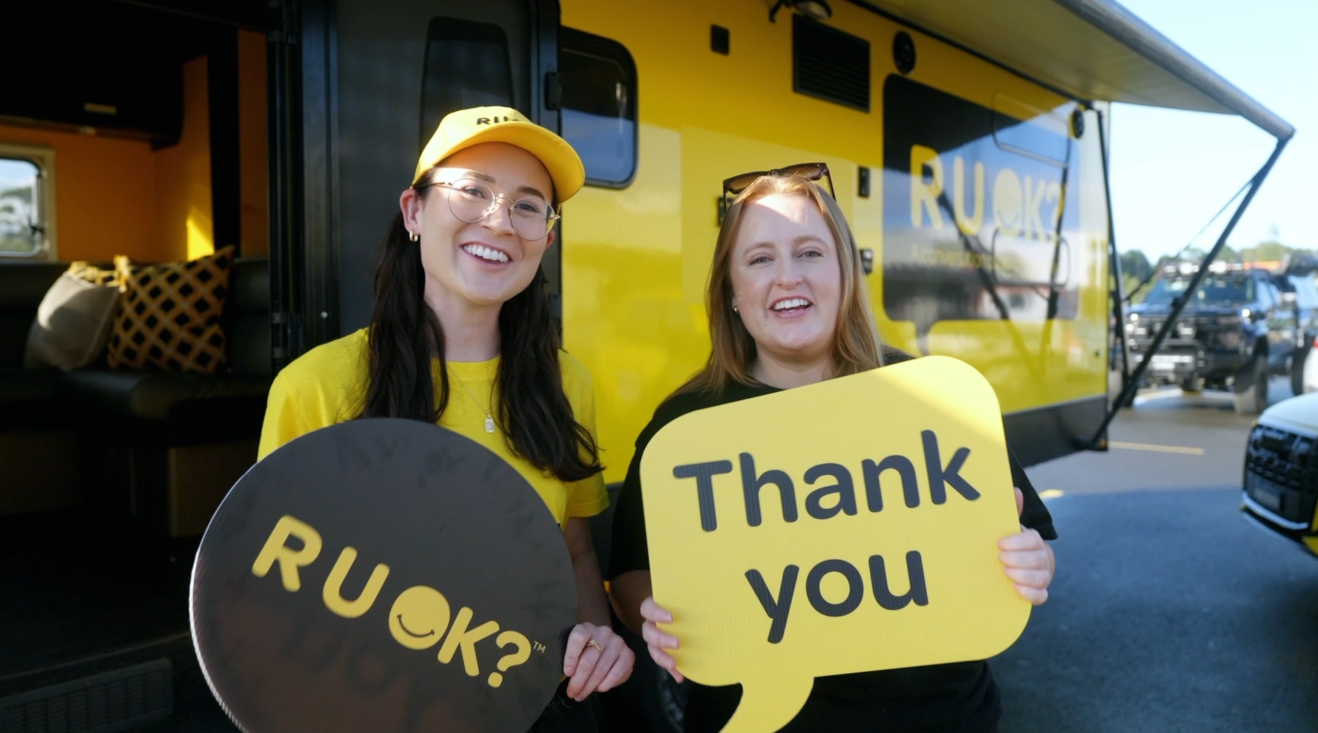 Two people in R U OK? yellow t shirts hold up signs saying 'R U OK?' and 'Thank you'.