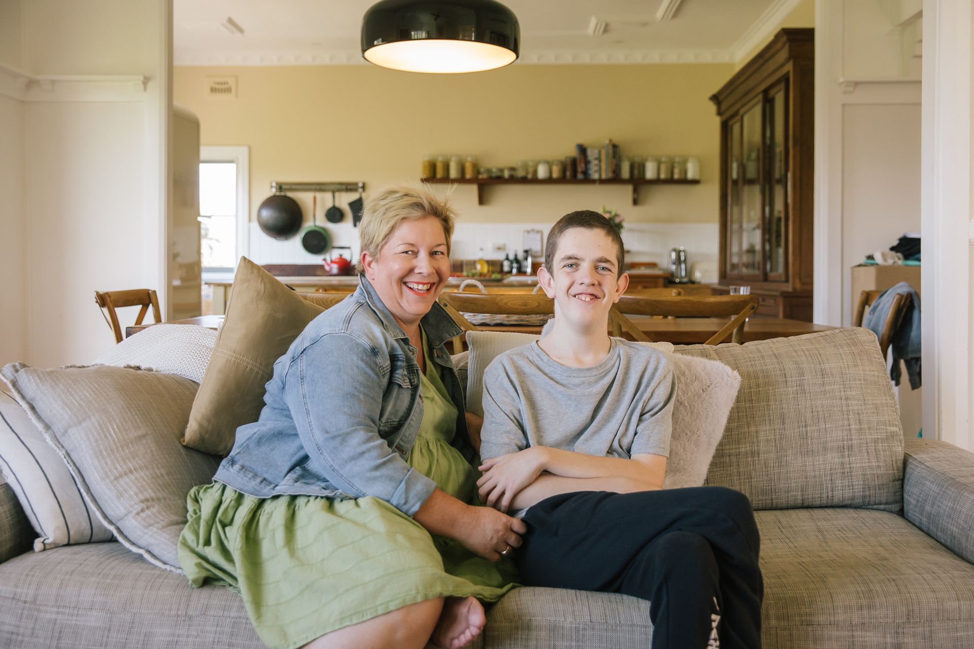 A woman and younger boy sit on a couch in a house.