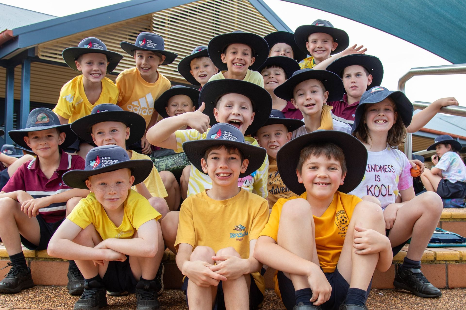 Students in hits and yellow uniforms smile.