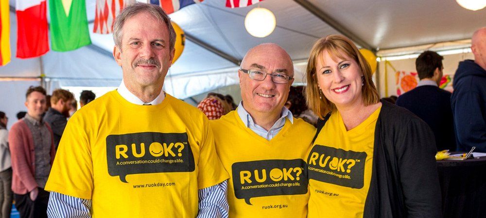 Group of people in the workplace smiling with R U OK? Signs