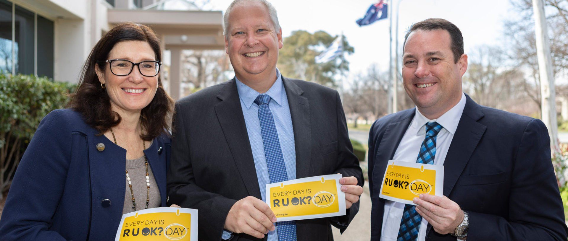 Group of people in suits smiling with R U OK? Signs