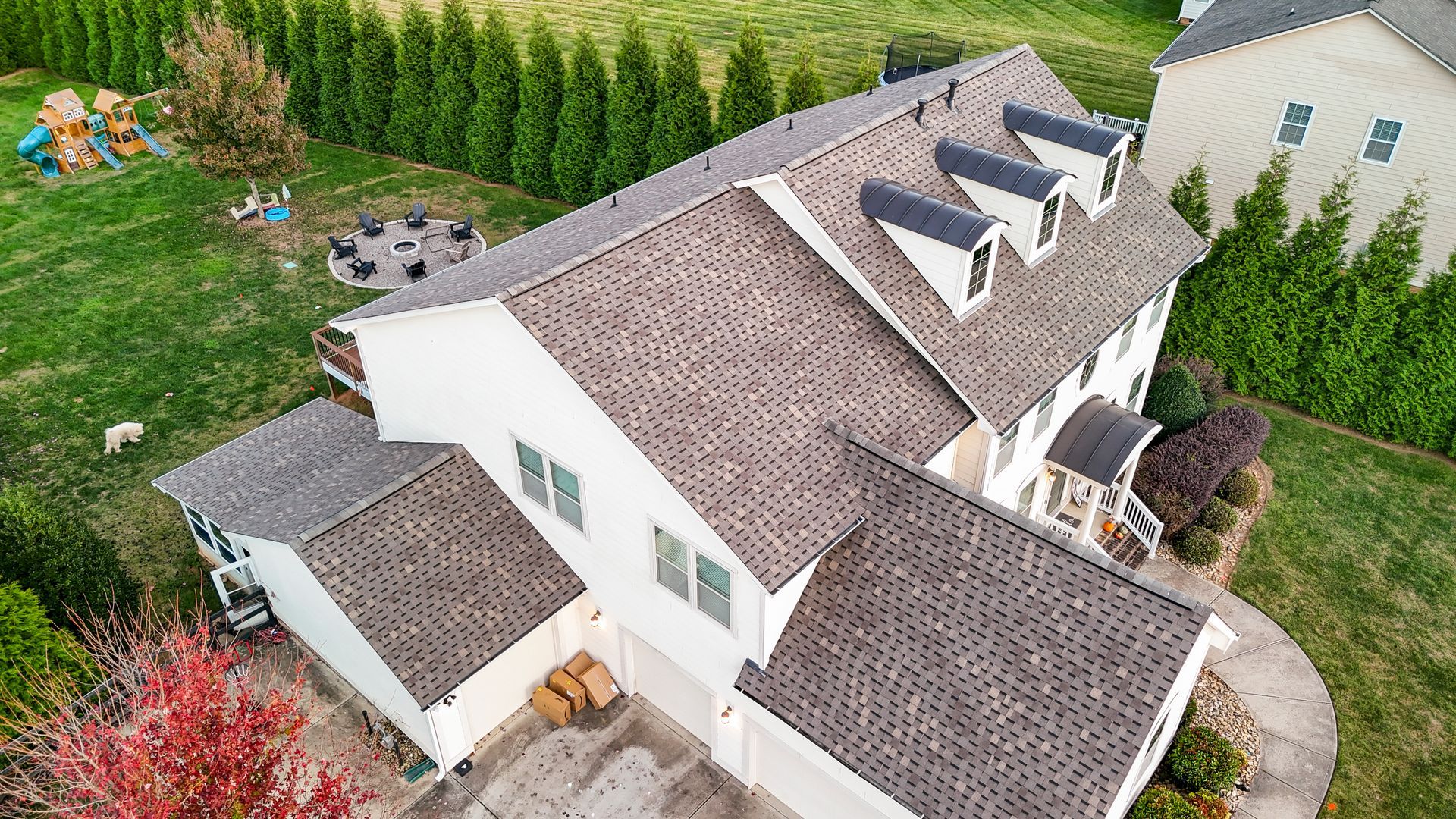 Overhead view of a white two-story house with a brown shingle roof, green lawn, and trees.