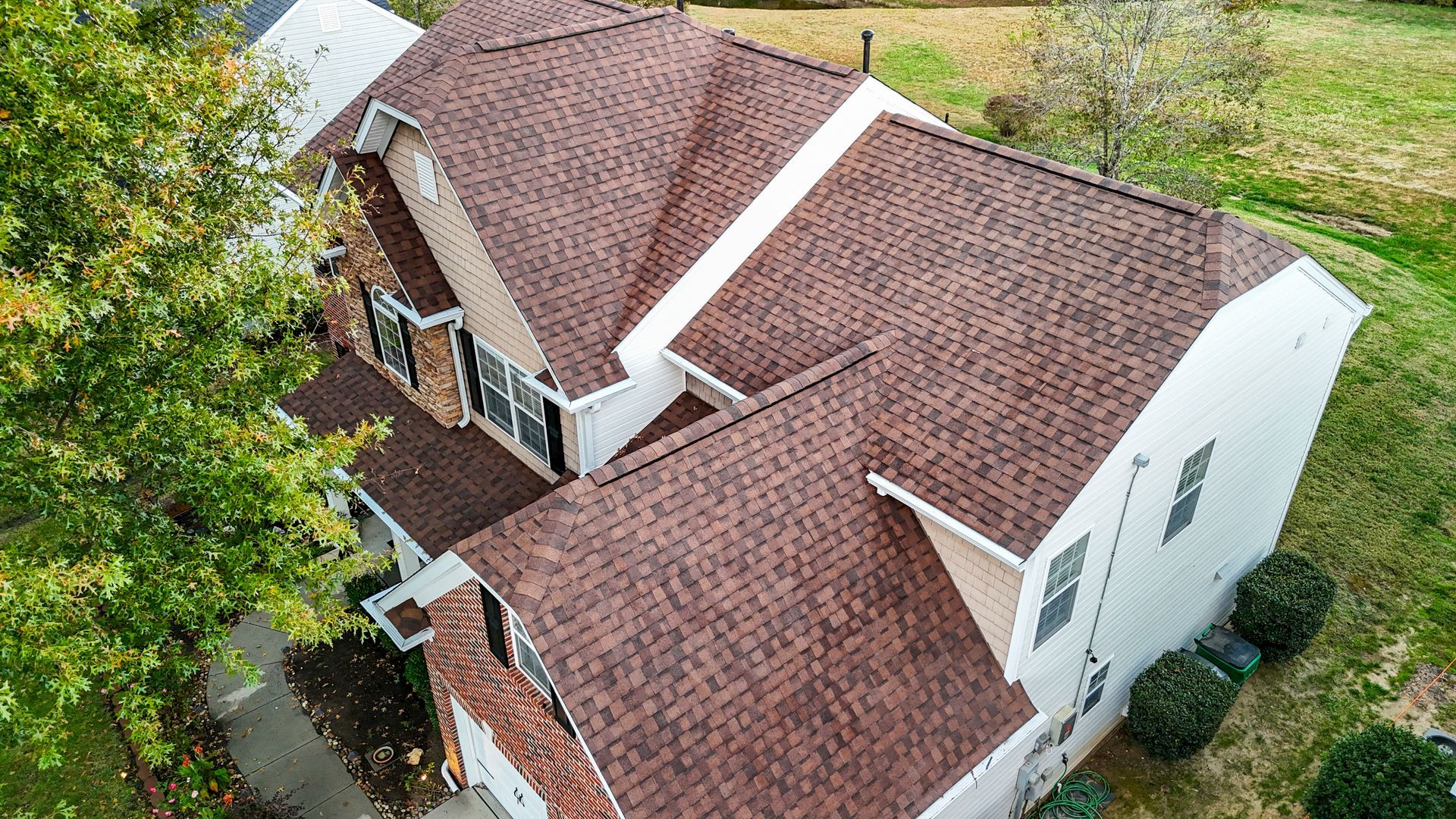 Brown roof on a white house with surrounding greenery.