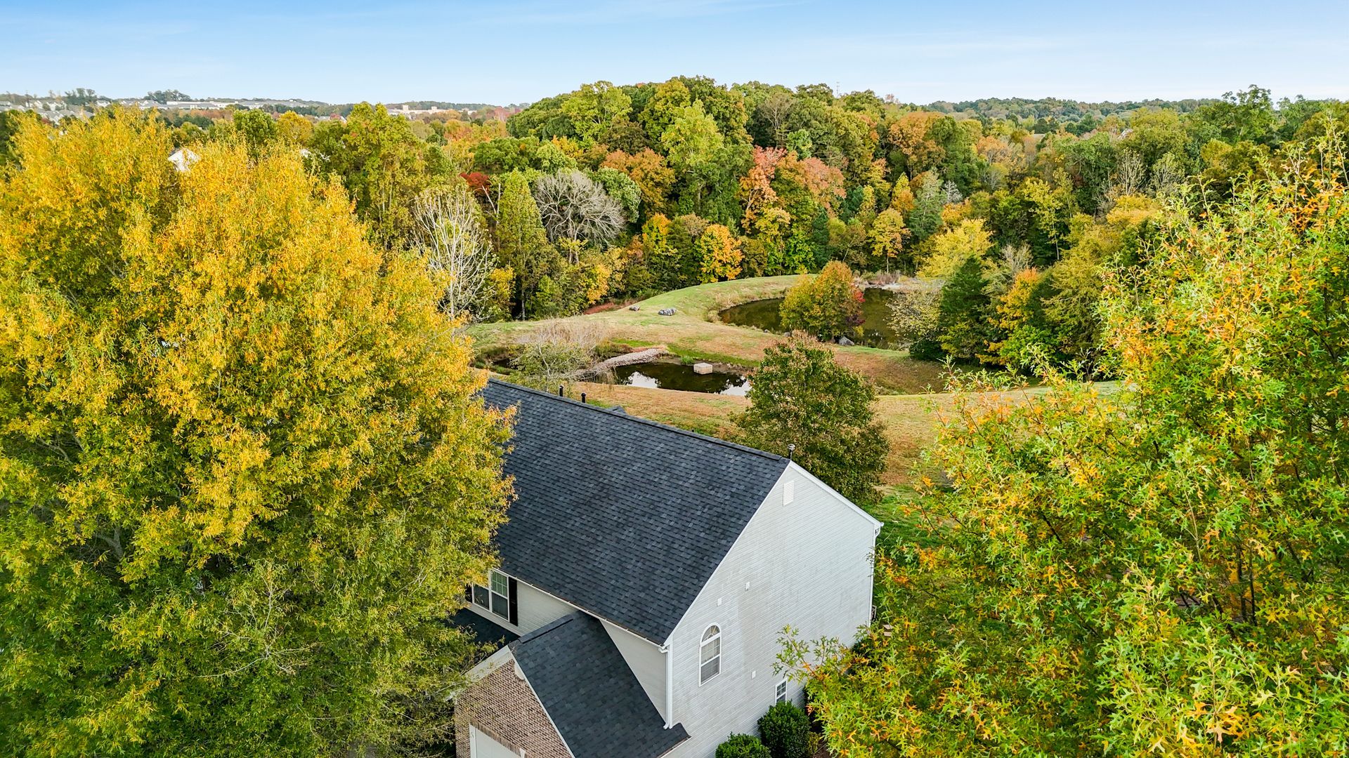 White house with dark roof surrounded by autumn trees and a pond.