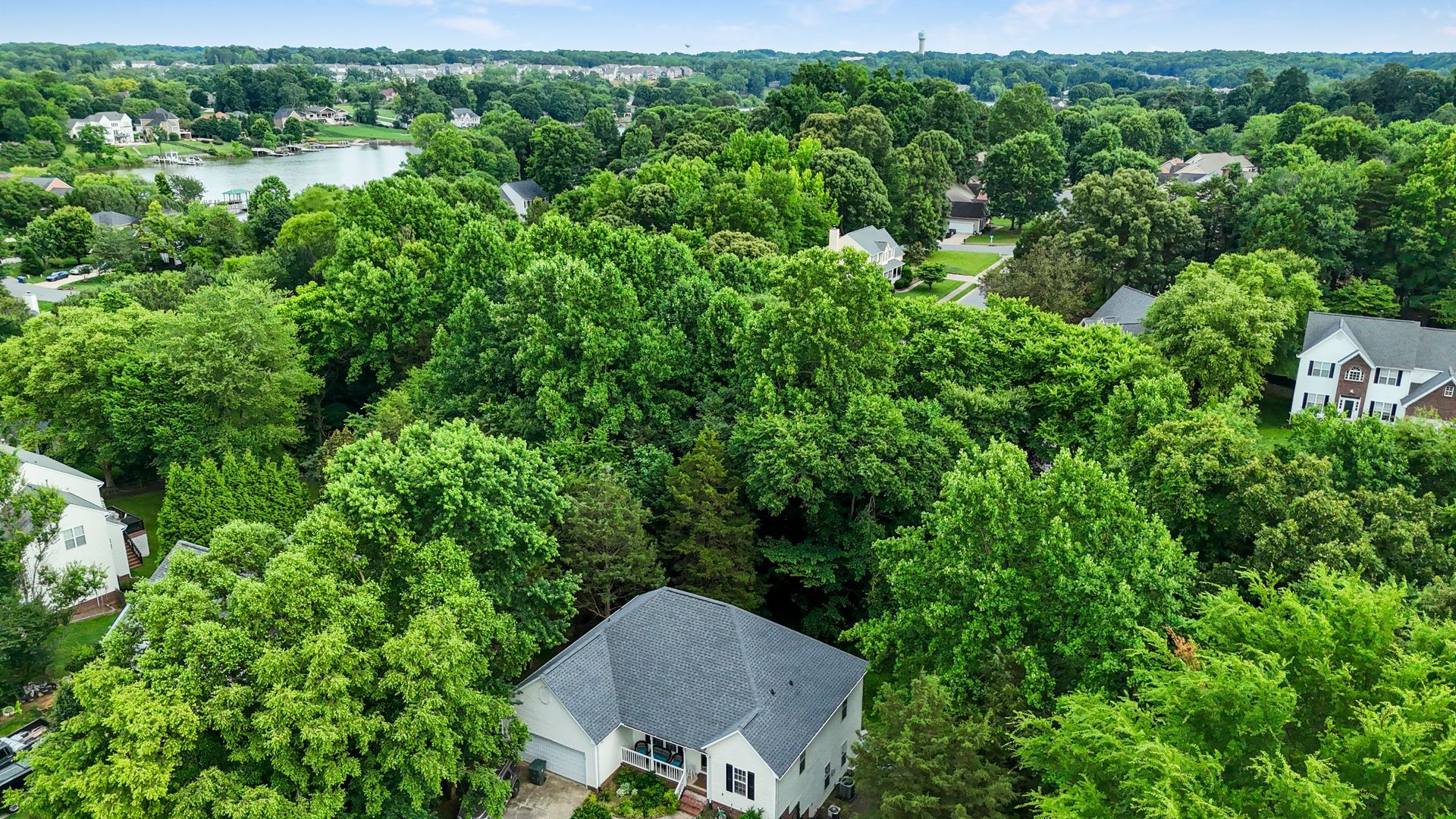 Aerial view of a suburban neighborhood with houses nestled among lush green trees, near a lake.