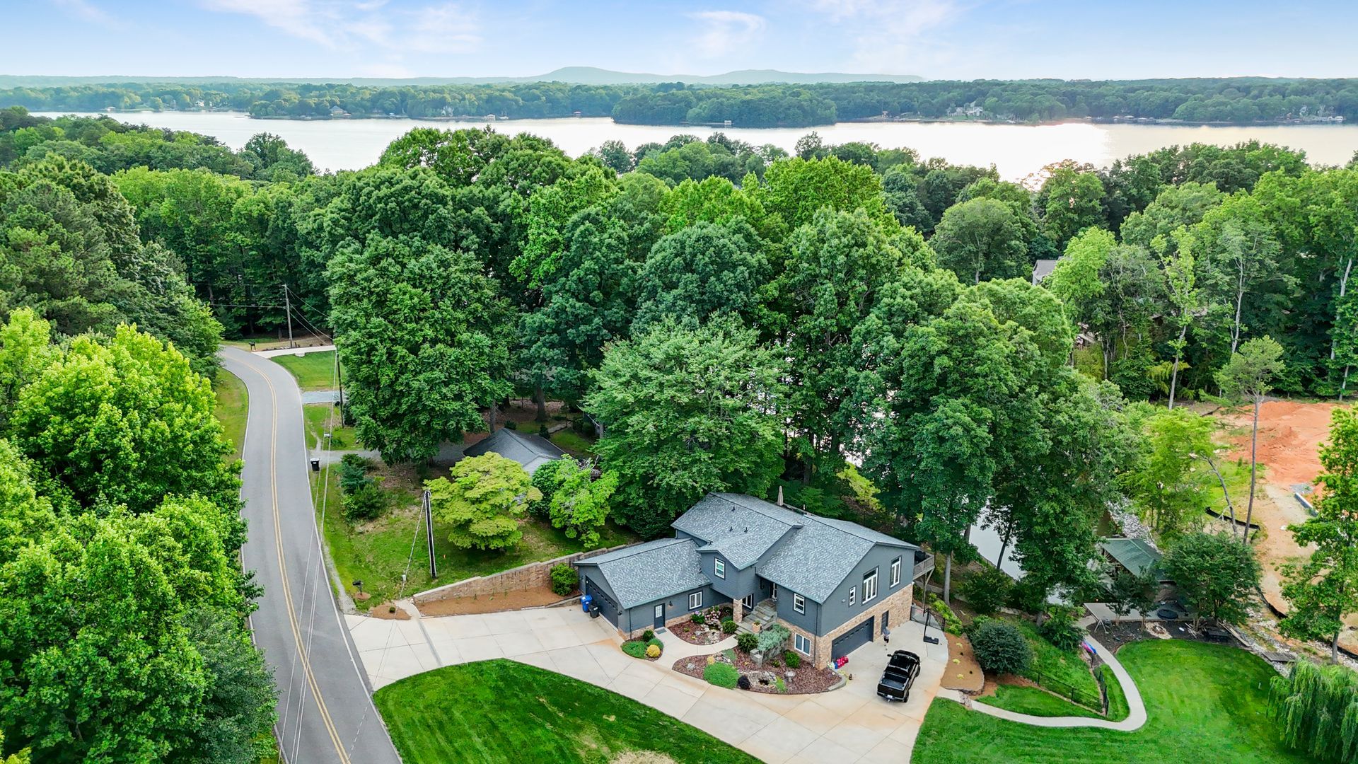 Aerial view of a gray house with a lake in the background, surrounded by lush green trees.