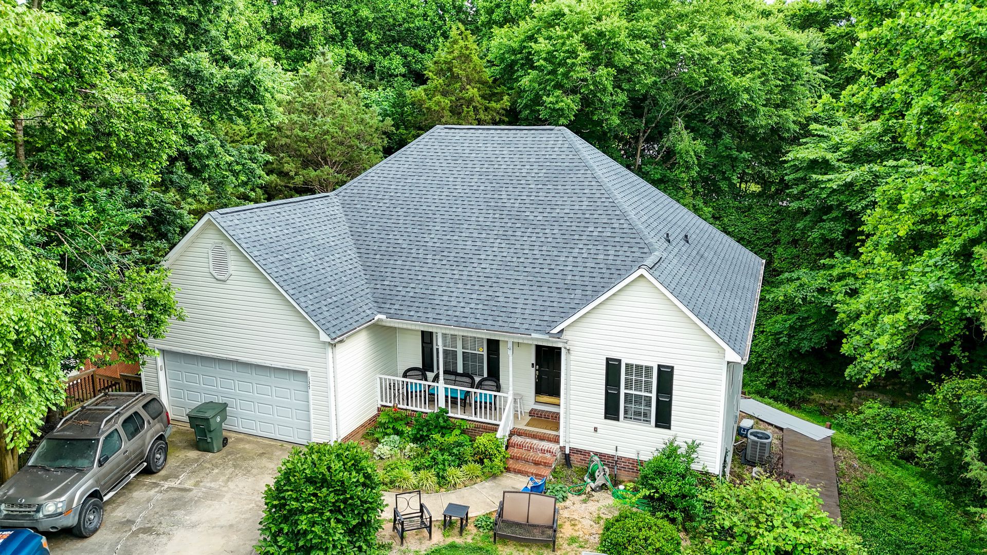 White house with gray roof surrounded by trees and a car in the driveway.