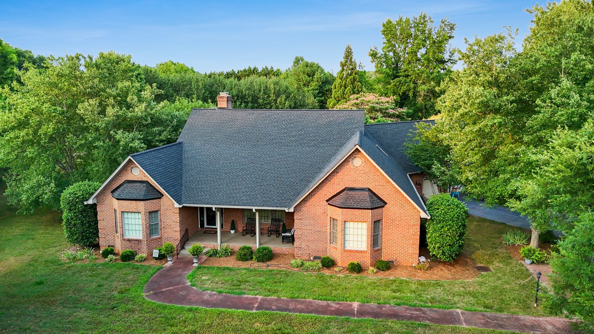 Stone house with dark roof and landscaping, surrounded by trees.