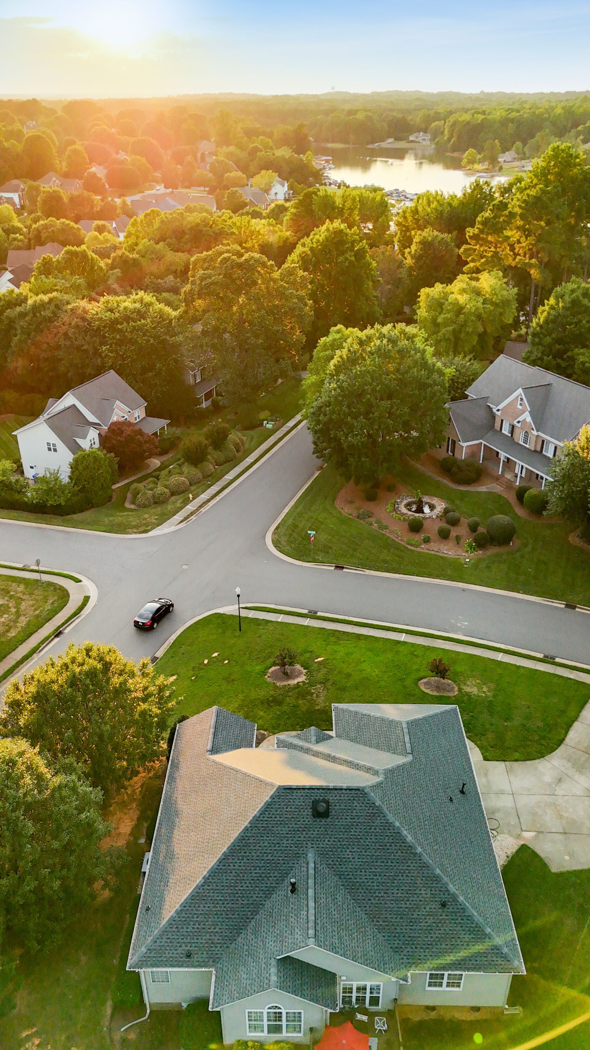 Aerial view of a suburban neighborhood at sunset; houses, trees, and a road.
