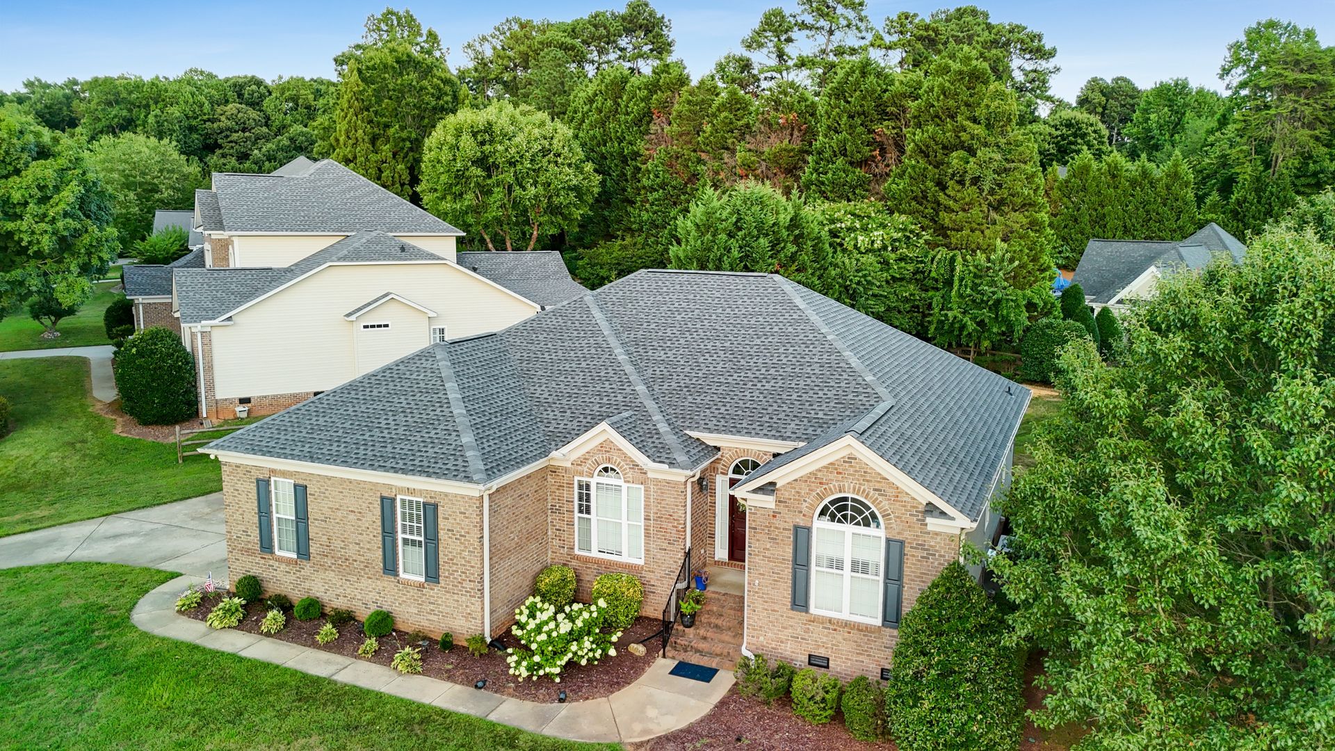 Brick house with dark roof and landscaping, surrounded by trees.