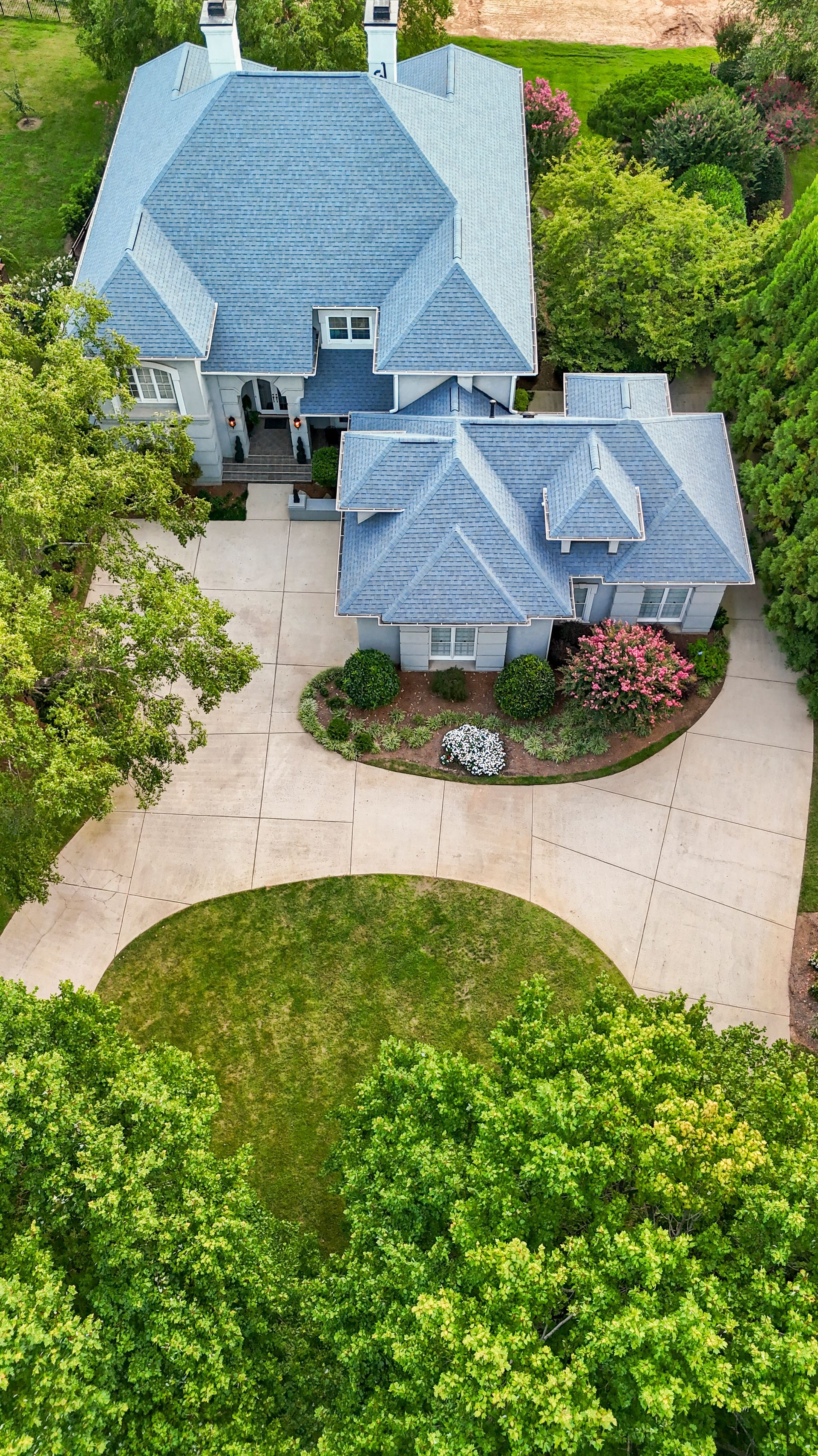 Aerial view of a gray house with blue roof and circular driveway. Green trees surround the property.