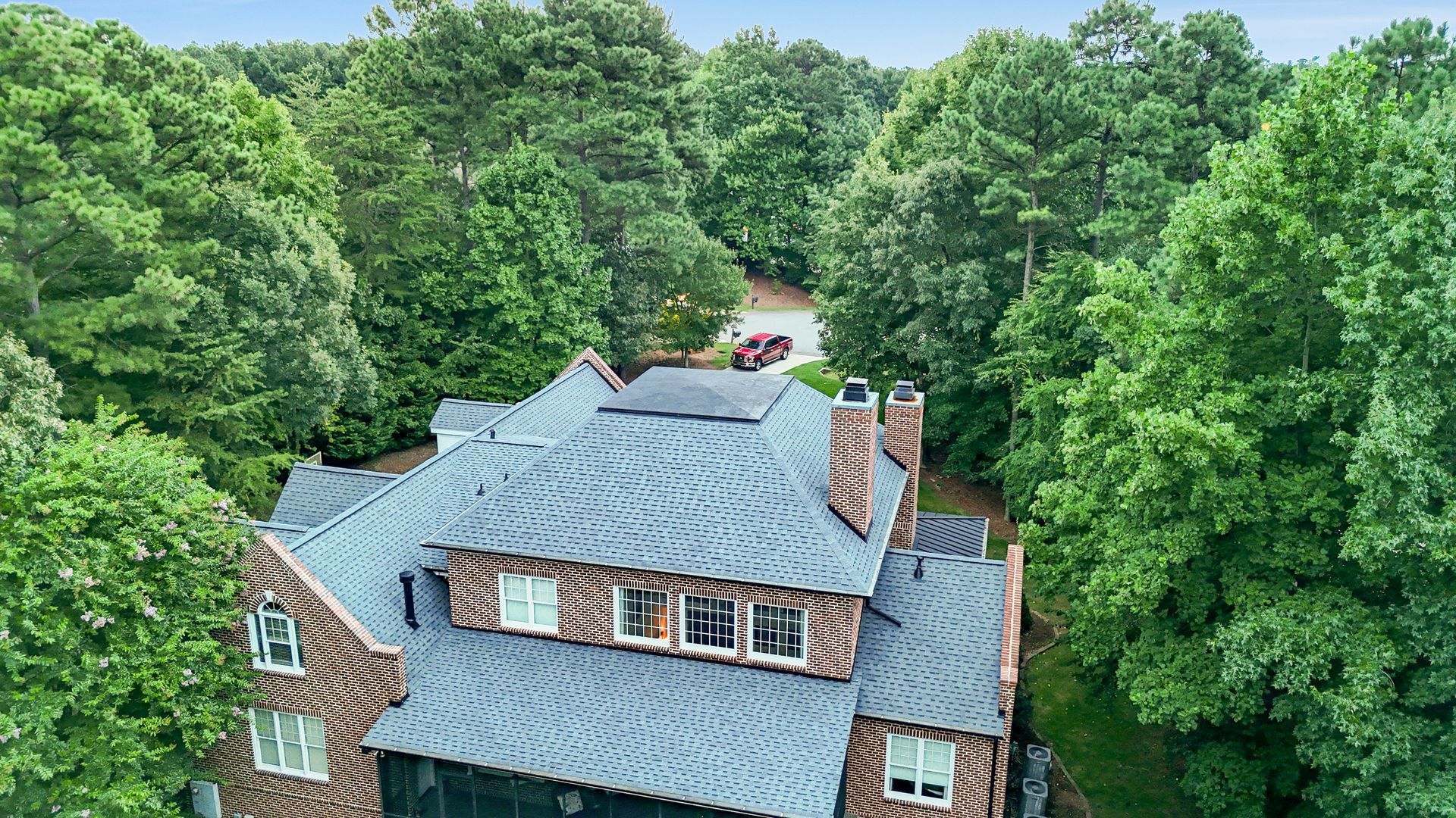 Overhead view of a house with a patterned roof and chimney surrounded by trees.