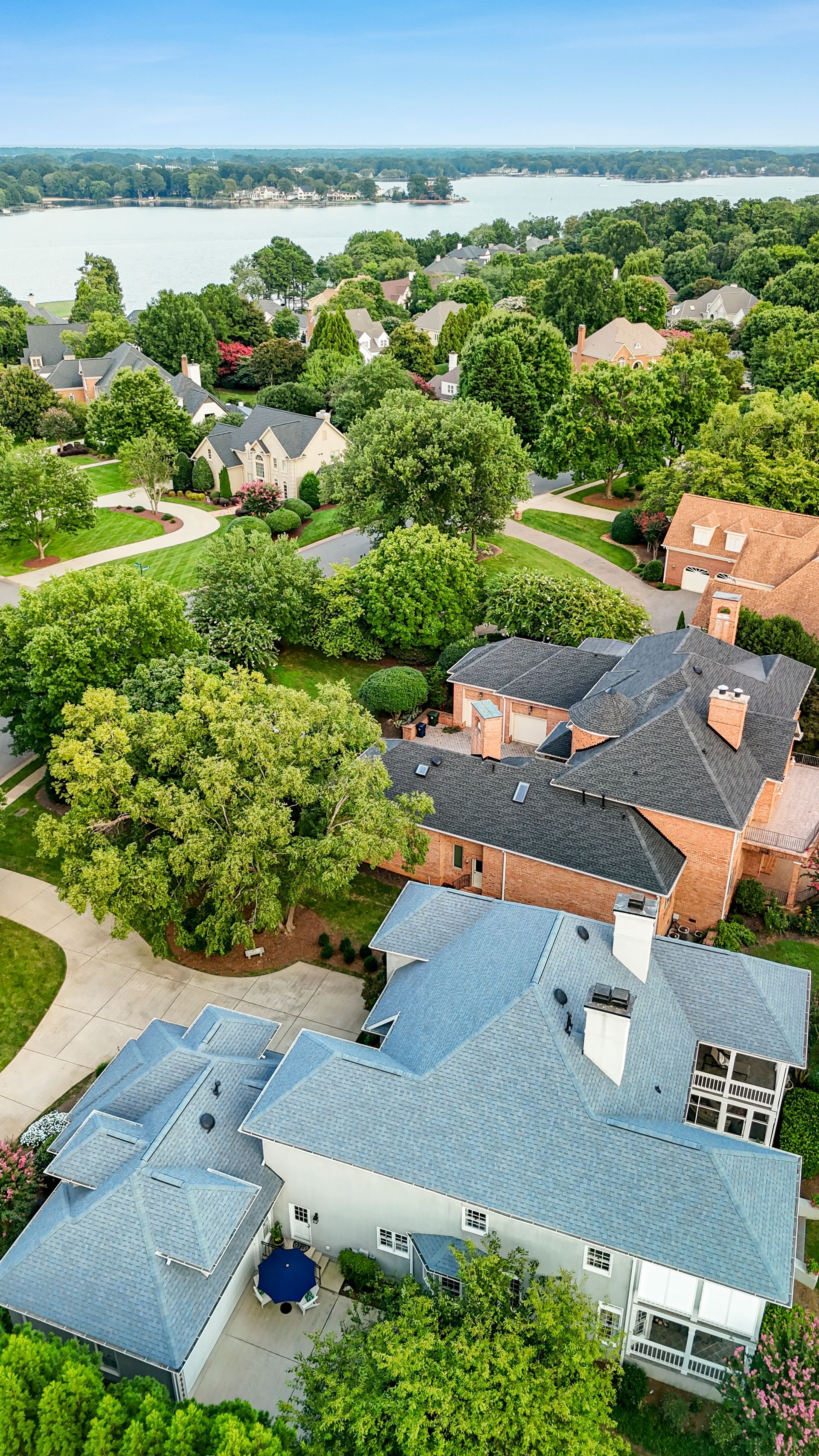 Aerial view of upscale homes with lush greenery, blue roofs, and a lake in the background.
