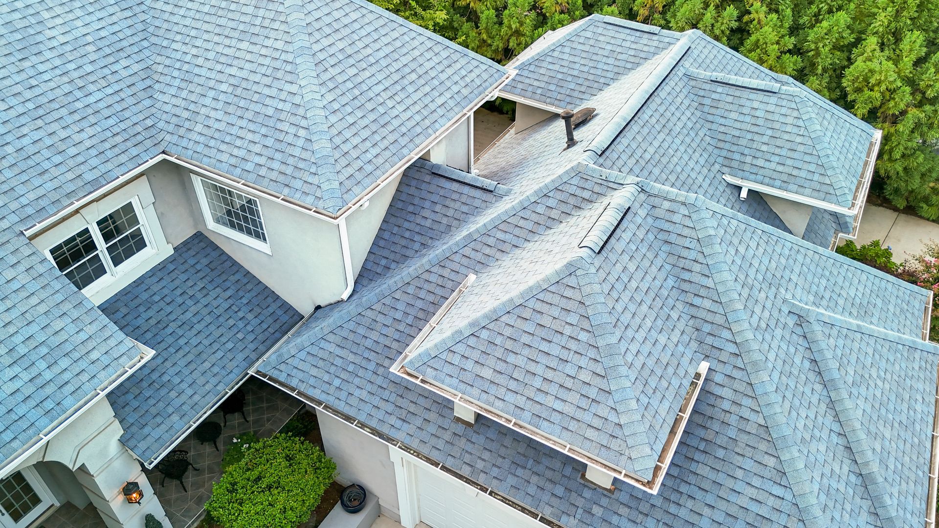 Aerial view of a house with a gray shingled roof, light gray exterior, and surrounding greenery.