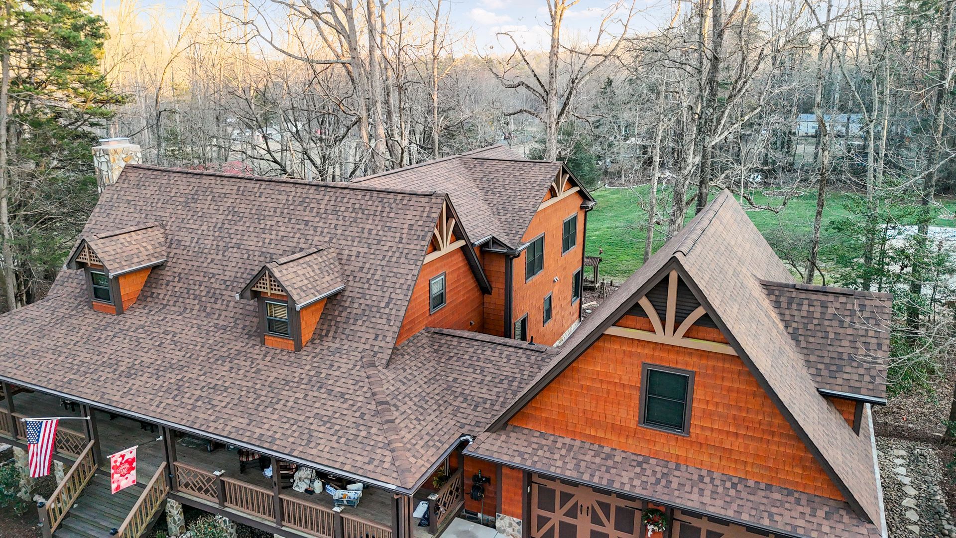 Wooden cabin with brown roof and American flag. Surrounded by trees.