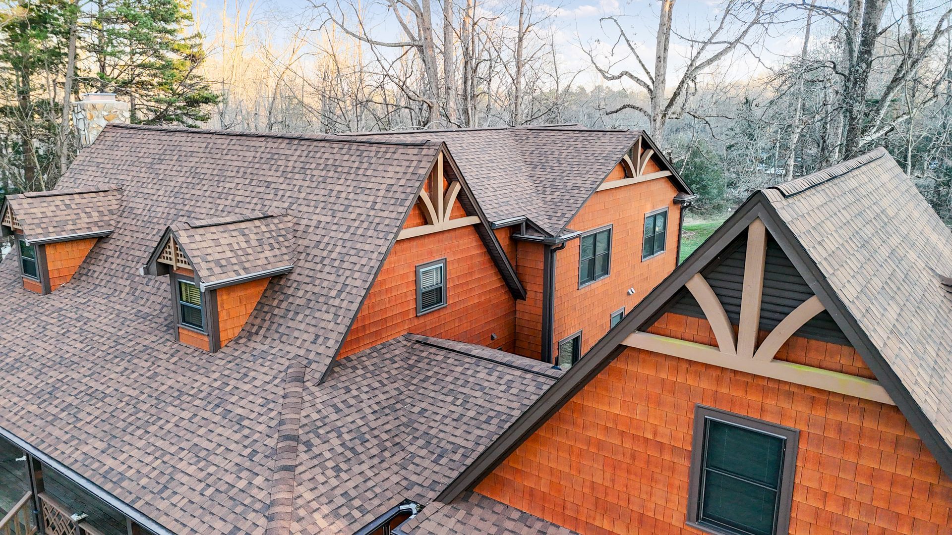 Brown shingle roof house with orange siding, dormers, and trees in background.