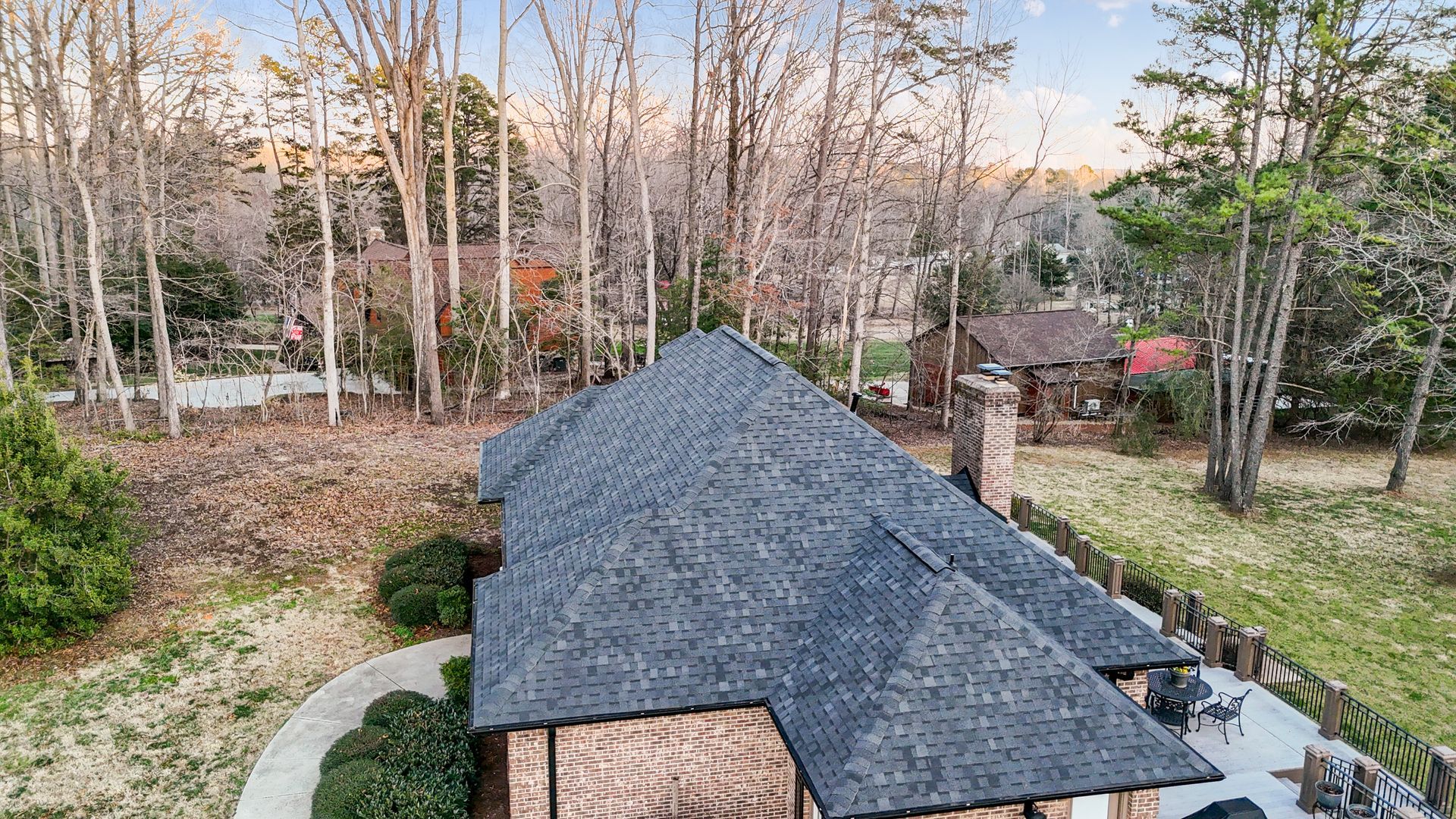 Aerial view of a home with a dark gray roof surrounded by trees and a brown brick exterior.
