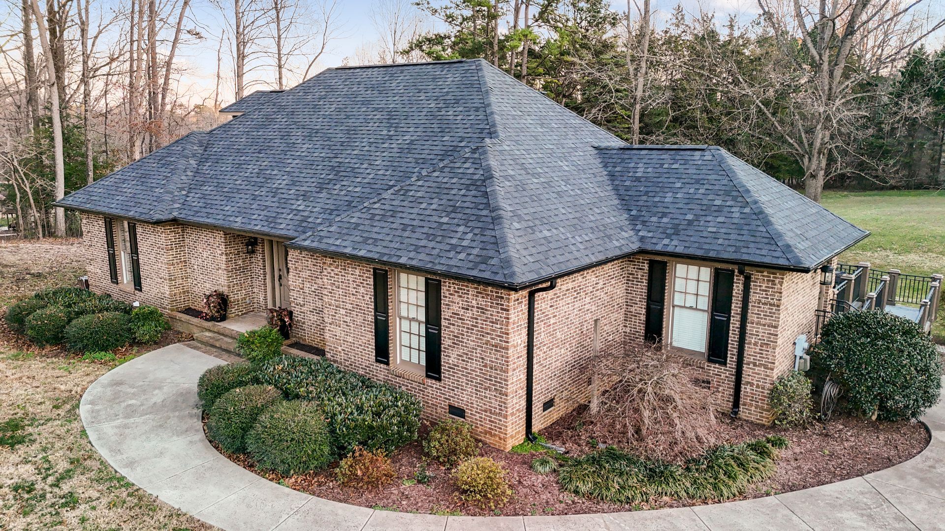 Brick ranch house with a dark shingled roof, landscaping, and a curved walkway.