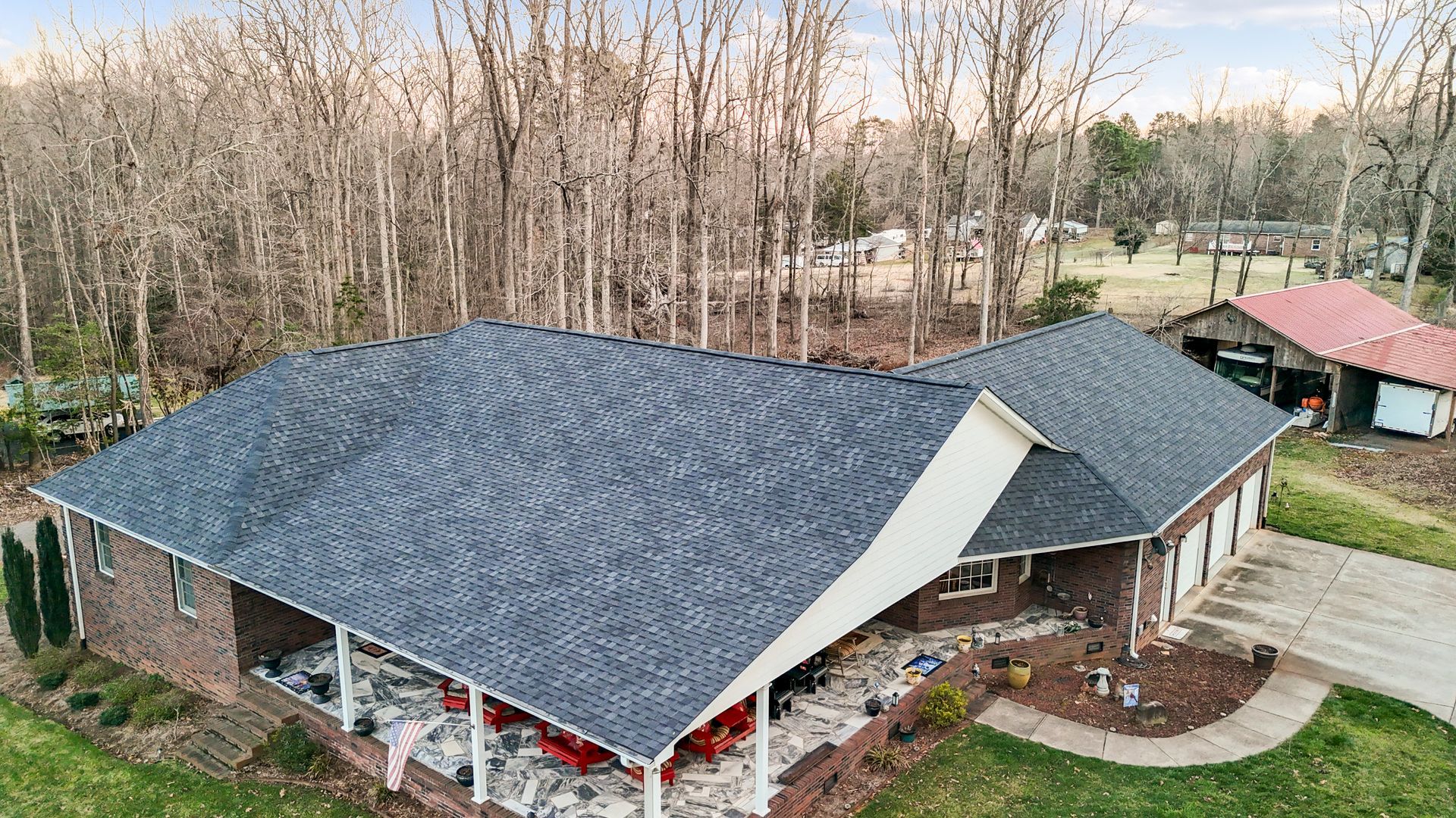 A brick house with a dark gray shingle roof, surrounded by trees in a rural setting.