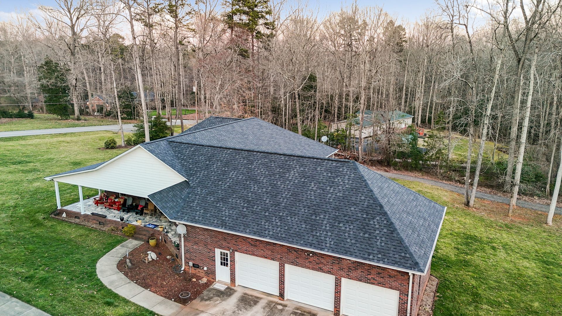 House with dark roof, white porch, three-car garage, surrounded by trees.