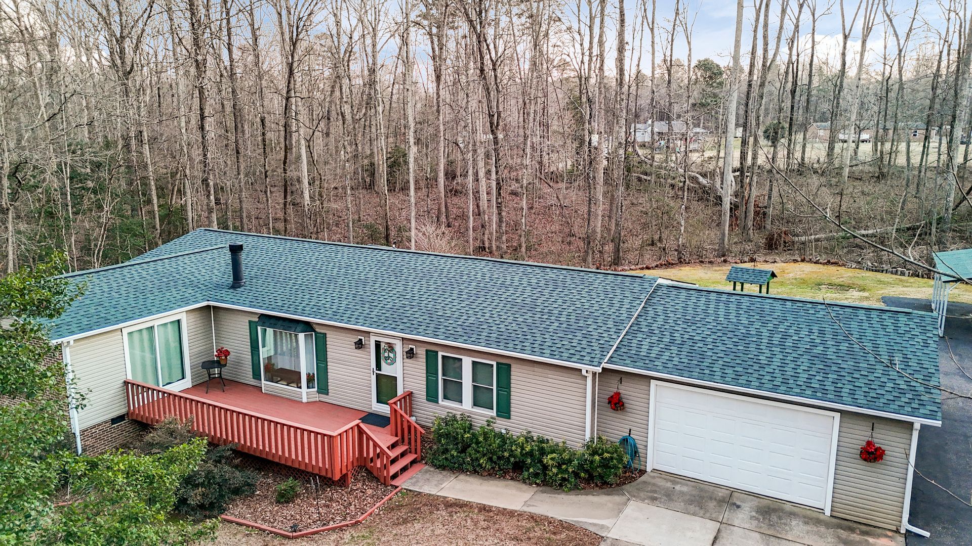 A single-story house with green roof, red porch, and a white garage, set against a backdrop of bare trees.