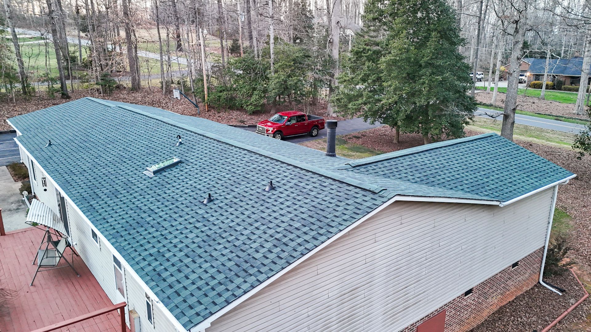 Overhead view of a house with a teal shingled roof, red car in driveway, and surrounding trees.