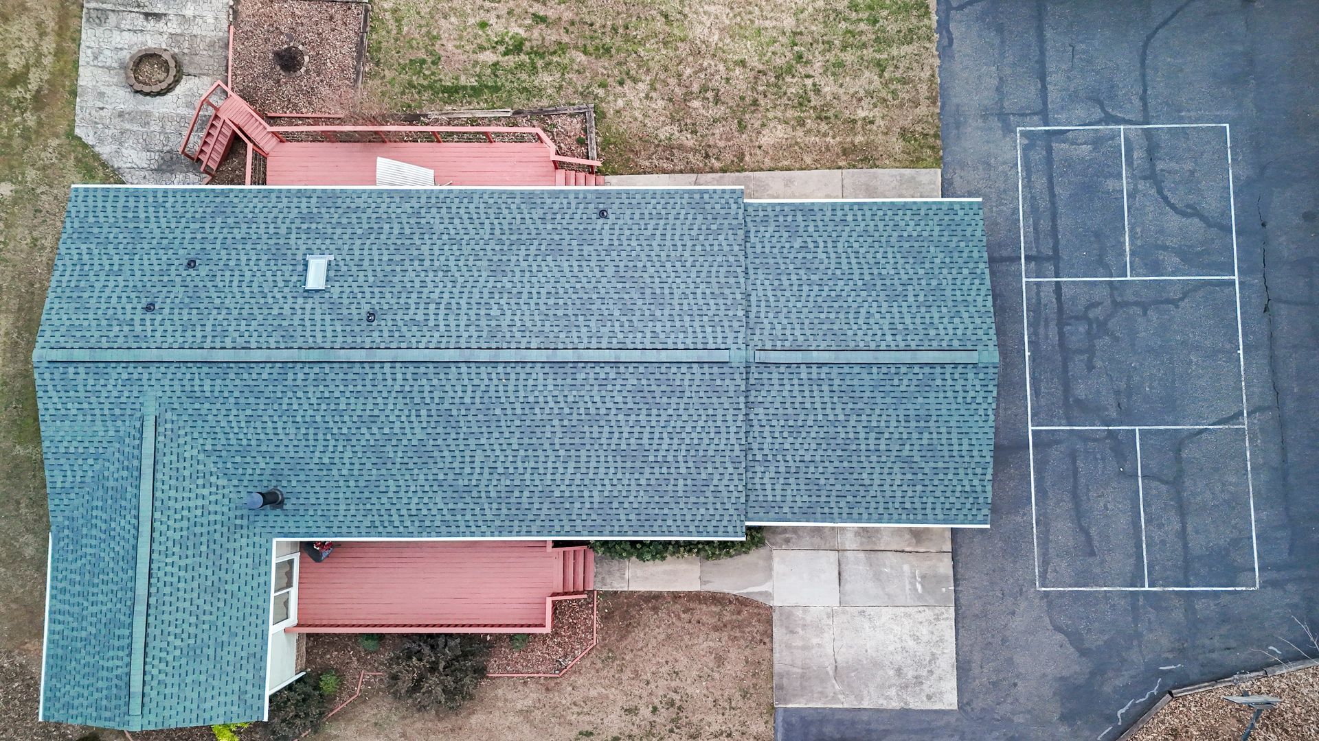 Aerial view of house with green roof and red deck, next to a paved area with white lines.