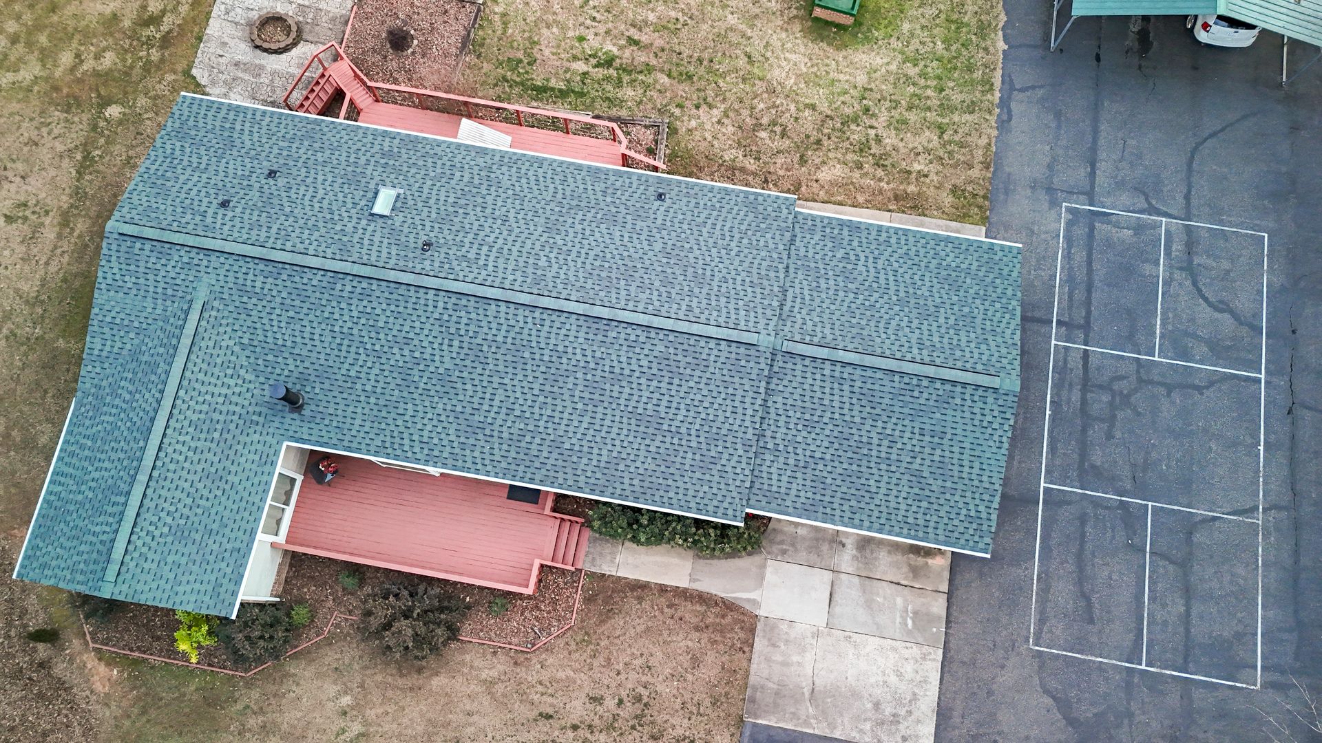 Aerial view of a teal-roofed house with a red deck and a driveway with white markings.