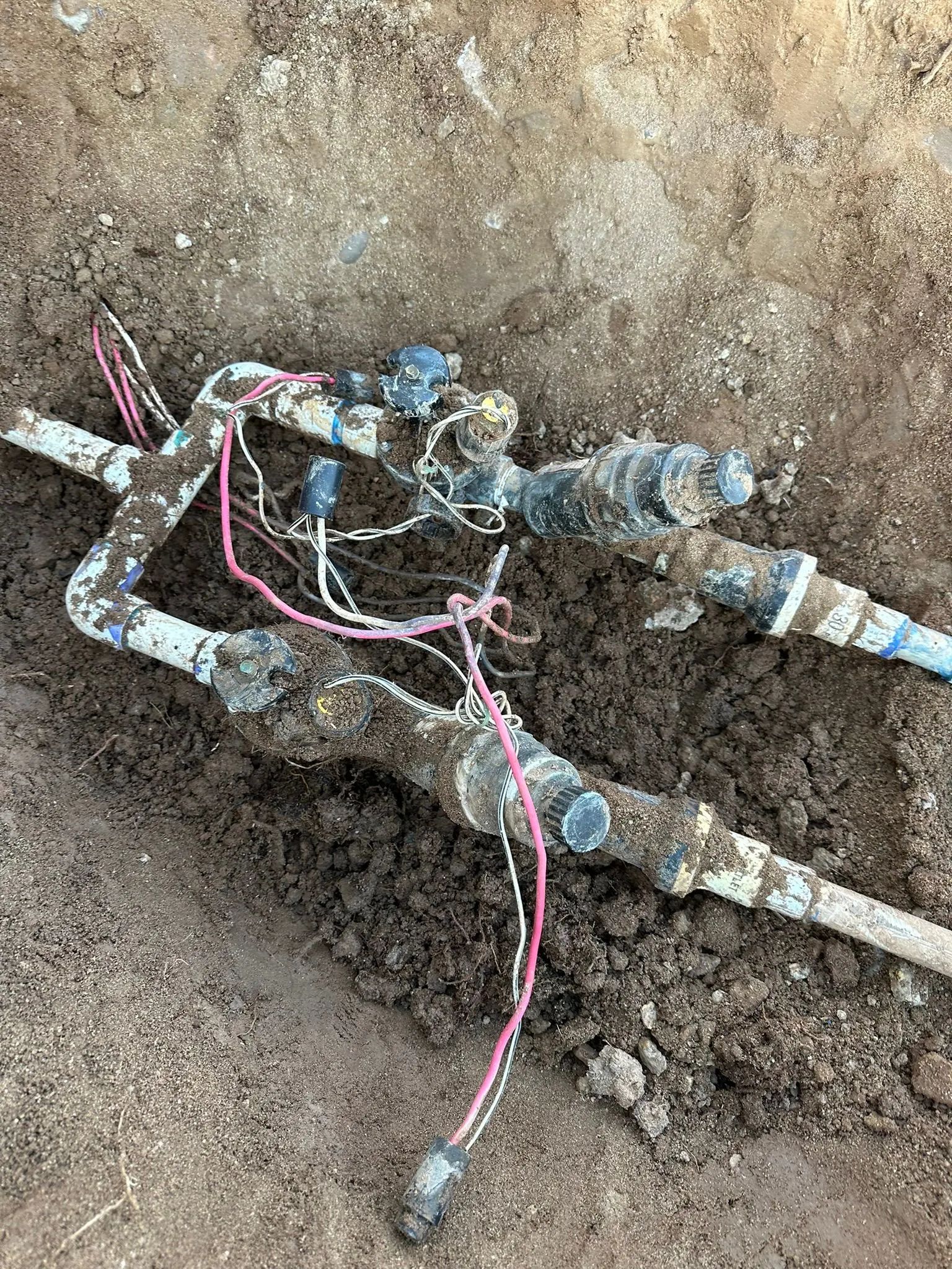 Irrigation system valves and pipes in a dirt trench, wires connected, various angles.